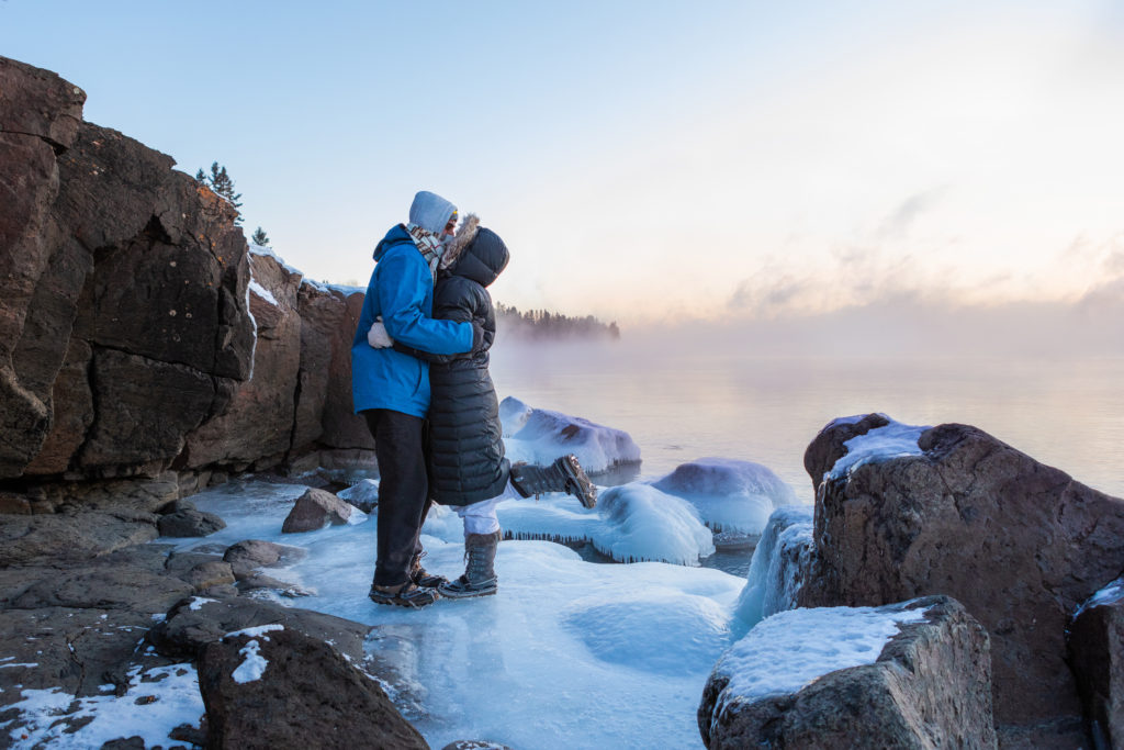 A couple snuggles close along the icy shores of lake superior during the winter