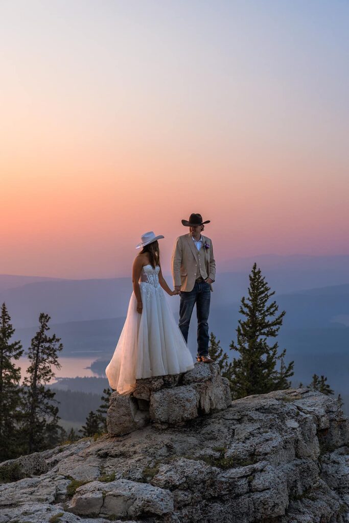 A couple in their wedding clothes stand at the top of a mountain during their adventure elopement in the Bighorn National Forest in Wyoming.