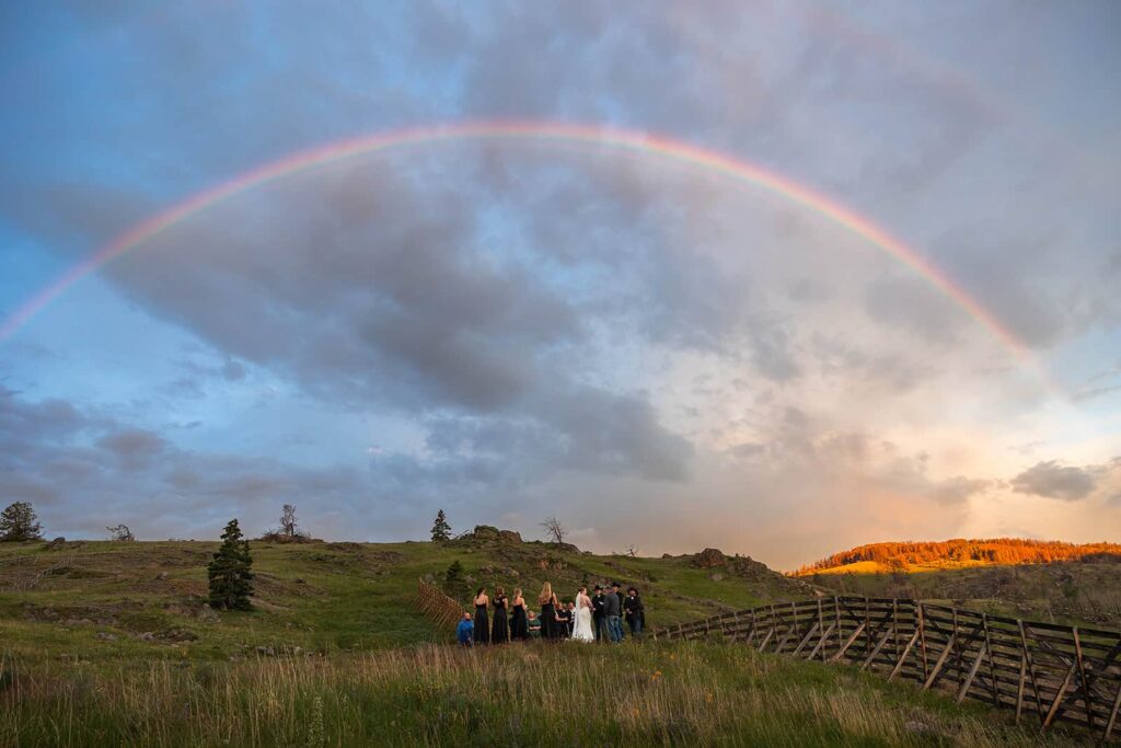 A full rainbow stretches across the sky during a sunrise wedding ceremony in Wyoming.