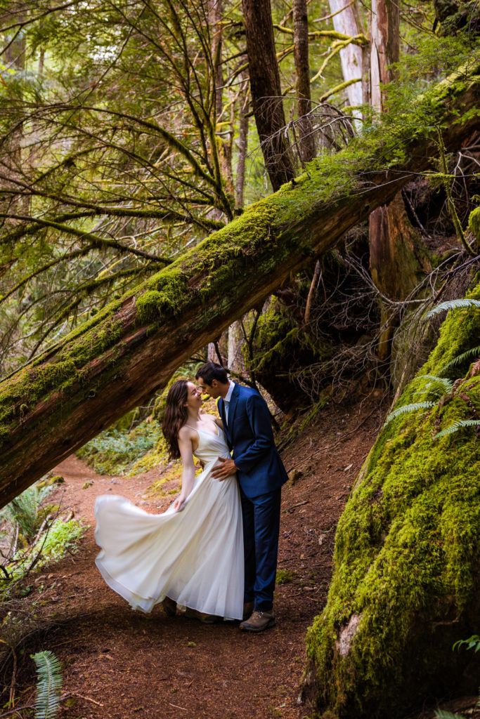 A bride tosses her elopement wedding dress in the air as she dances with her husband in a mossy Washington forest.