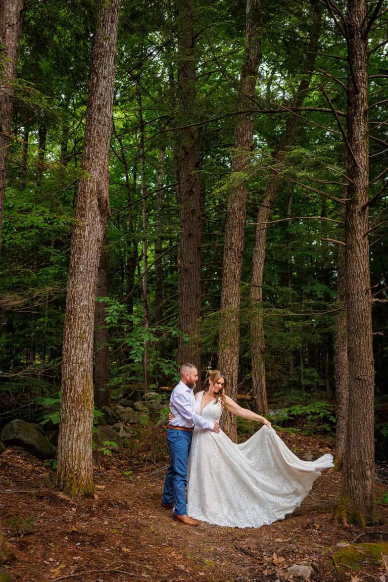 A bride swishes her elopement wedding dress in the forest while embracing her groom during their New Hampshire elopement.