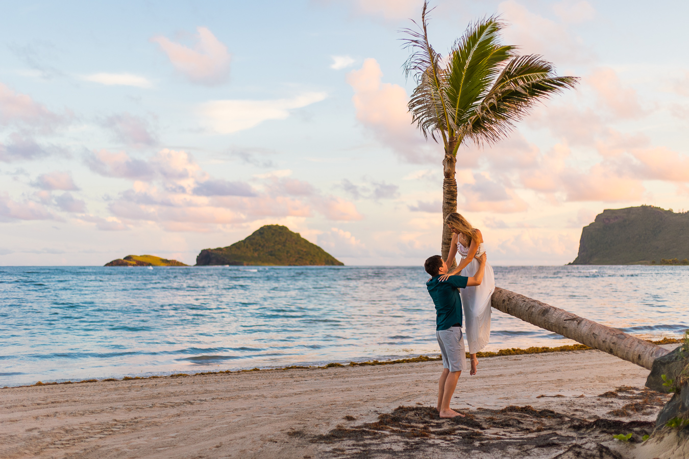 A groom helps his bride down from a palm tree during their tropical elopement so that she doesn't wreck her elopement dress