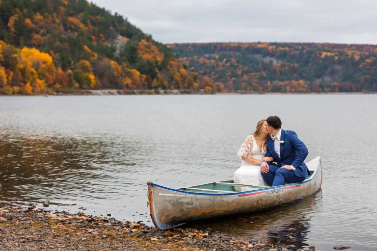 A bride and groom in their wedding clothes sit in a canoe during their elopement at Devil's Lake State Park. Canoeing is a fun and unique thing to do on your wedding day!