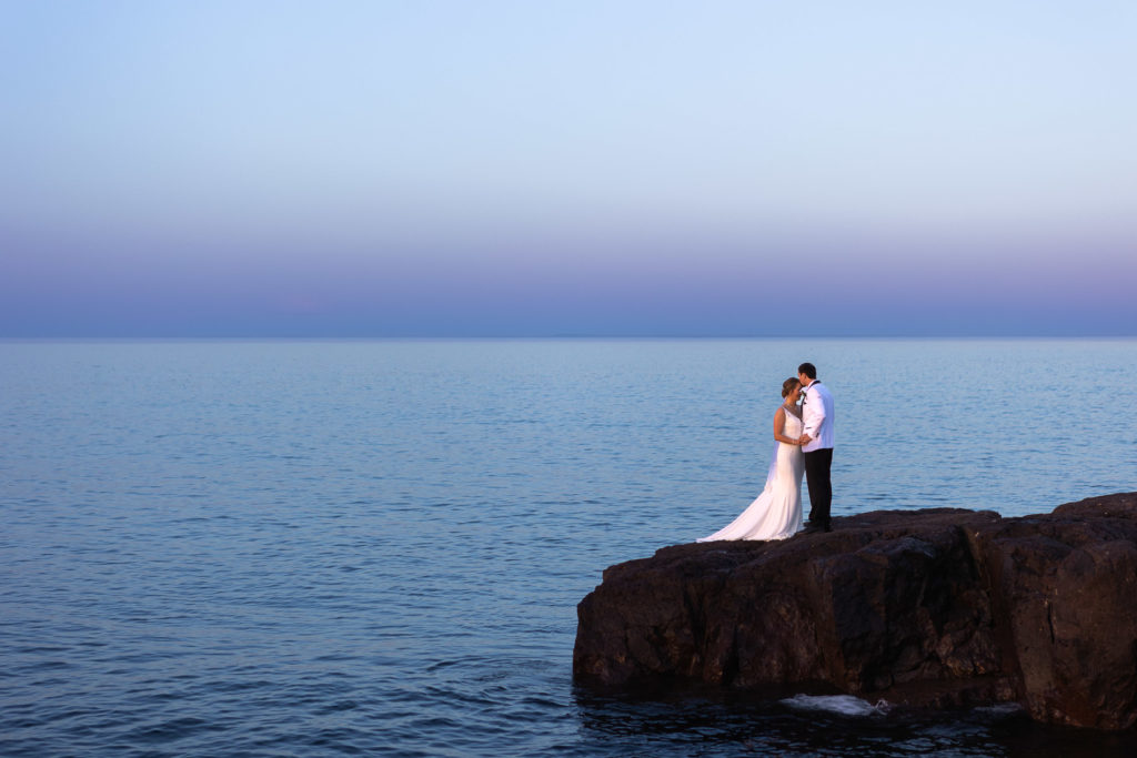 A groom kissing his bride's forehead on the rocky shore of lake superior during their Gooseberry State Park Intimate Wedding.
