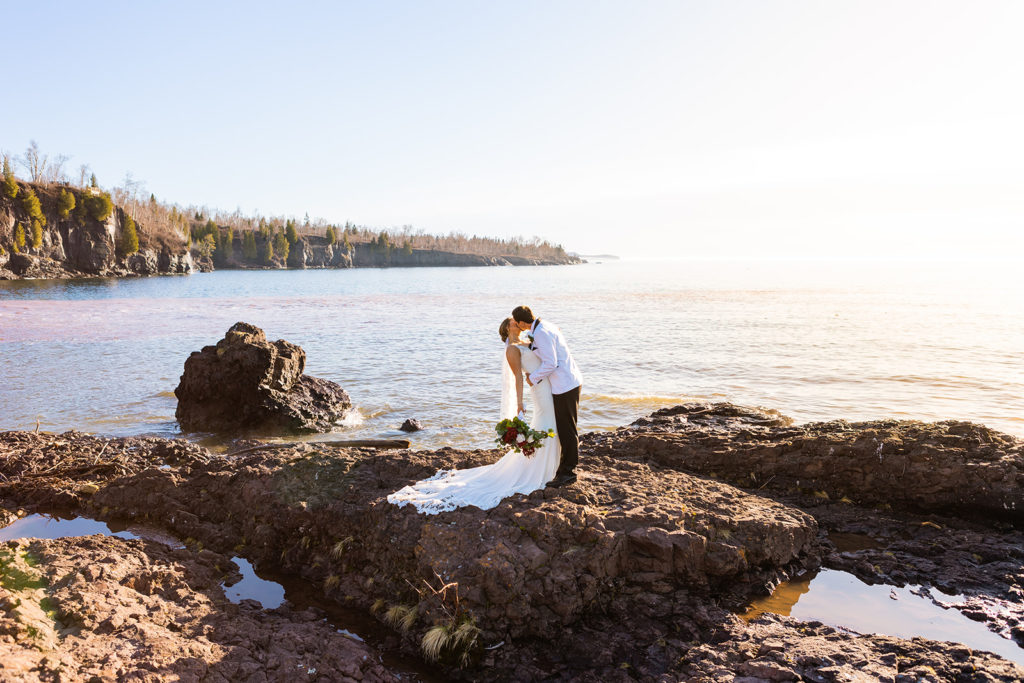 A couple kiss on the rocky Lake Superior shore during their north shore adventure elopement.