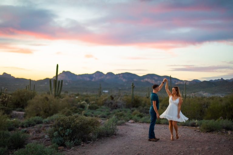 A couple dances in the last light of the sunset among the cacti of Lost Dutchman State Park during their engagement photos in Arizona.