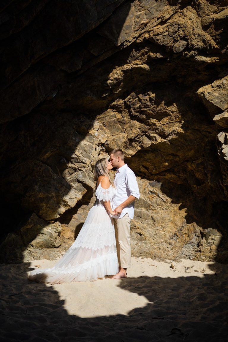 Hiking in their wedding clothes, bride and groom explore a cave on the beach during their big sur elopement.