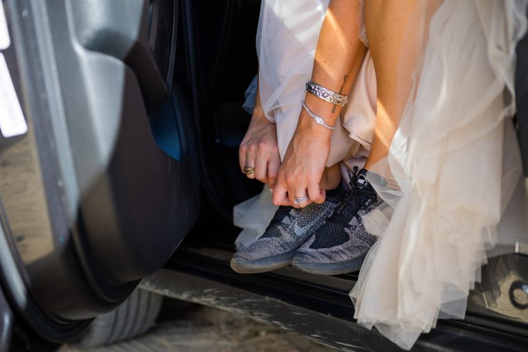 A bride ties her shoes while preparing to hike in her wedding dress for her adventure elopement.