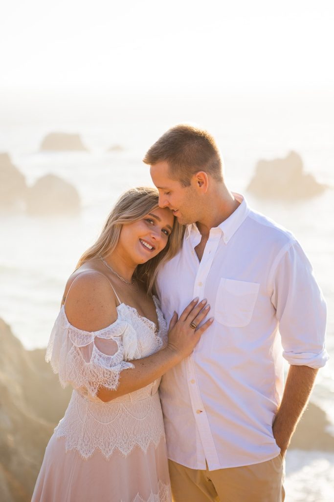 A groom smiles down at his bride during their elopement along the California Coast. The couple has stopped at one of the scenic pull-offs planned into their elopement timeline to take in the sights of the rugged coastline.