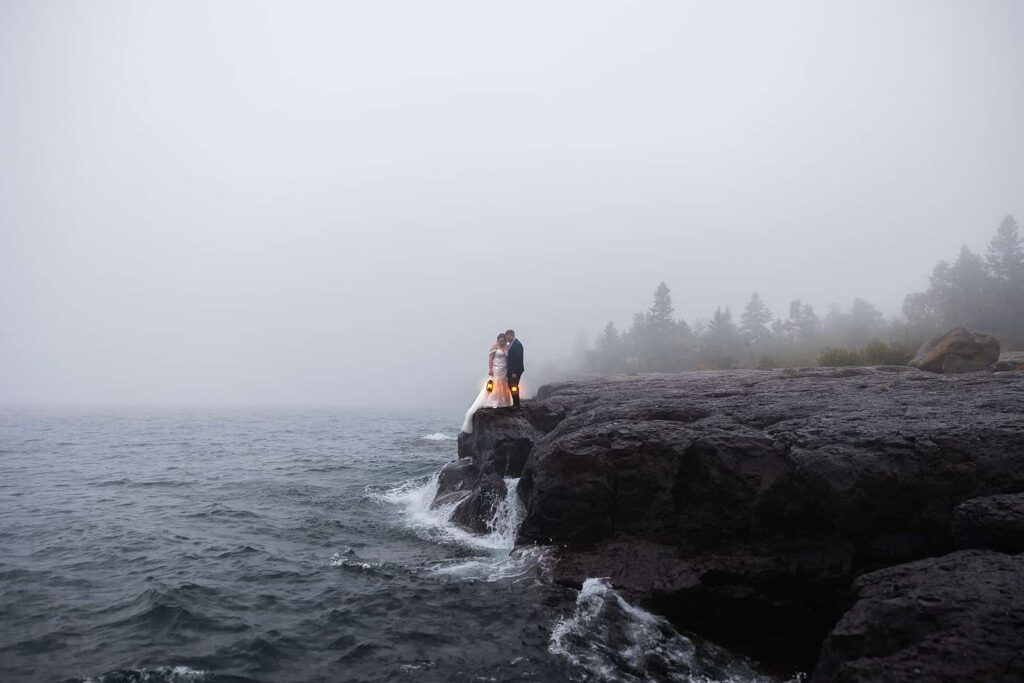 A bride and groom hold lanterns while standing on the shore of a stormy Lake Superior during their Midwest adventure elopement.