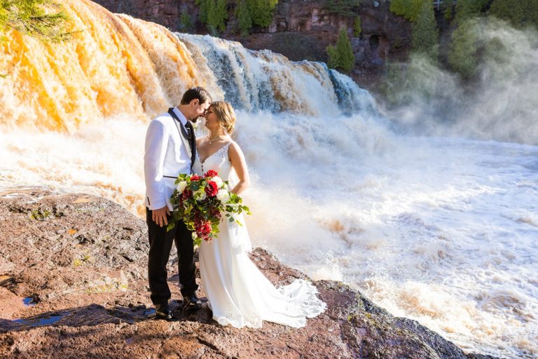 A bride and groom stand in front of Gooseberry falls during their elopement.