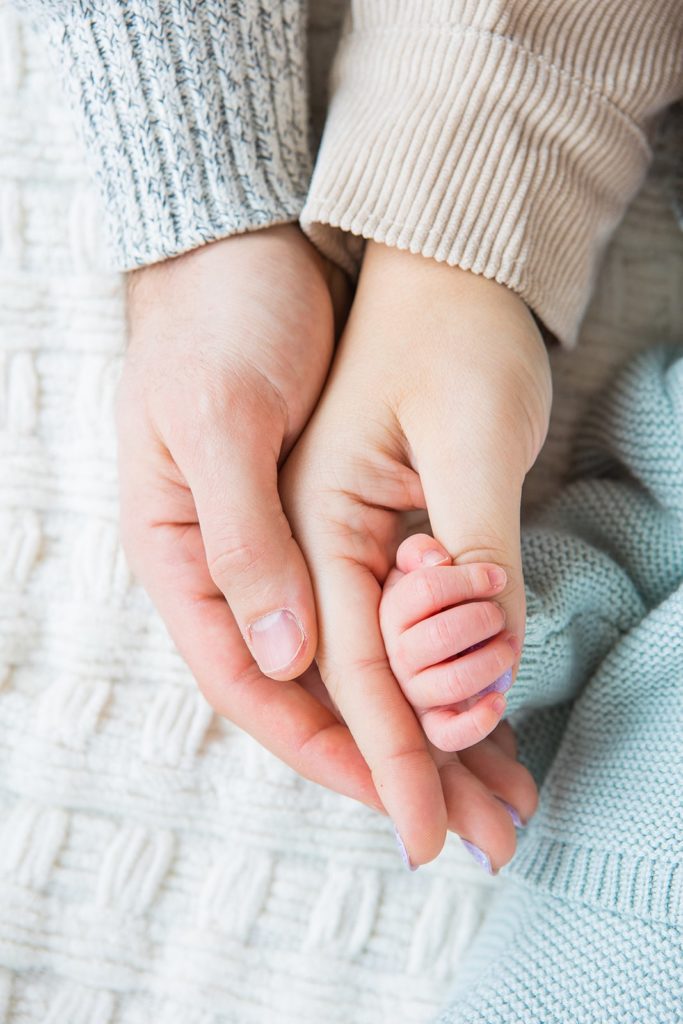 Two parents' hands cup the hand of their newborn baby during their lifestyle newborn session at their home in Minnesota.