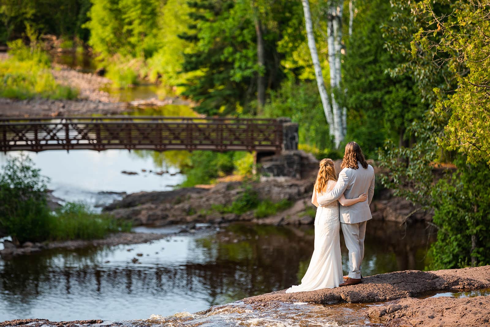 A bridge and groom stand together on their elopement day on a rocky cliff edge overlooking one of the many rivers flowing into Lake Superior along the North Shore.