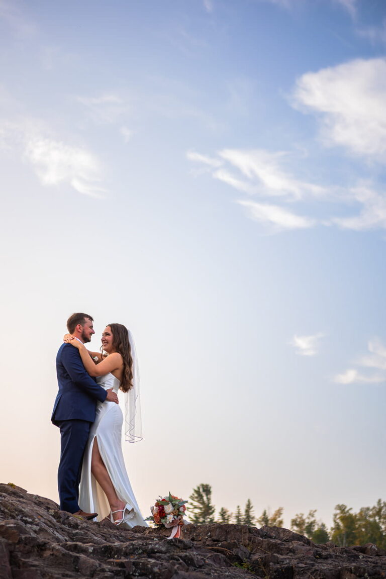 A couple stand on a cliff against a blue sky during their North Shore Minnesota Elopement.