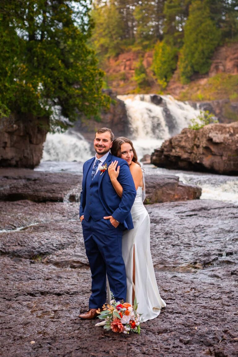 A couple stand in front of a waterfall during their North Shore elopement in Minnesota.