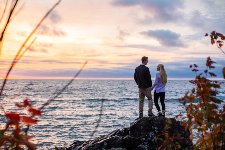A couple poses on a rock overlooking the sunrise on Lake Superior during their Tettegouche State Park engagement photos.