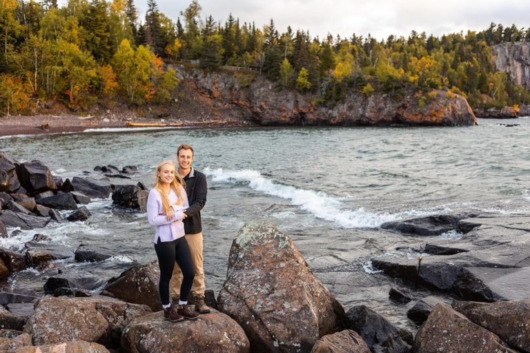 A couple poses on the rocky shore of Lake Superior during their engagement shoot at Tettegouche State Park in Minnesota.
