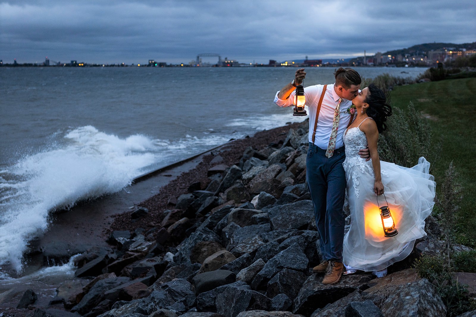 A couple kiss on the shore of Lake Superior in Duluth, MN as the waves crash along the rocks. With comfortable temperatures and beautiful scenery, fall is one of the best times to elope in Minnesota!