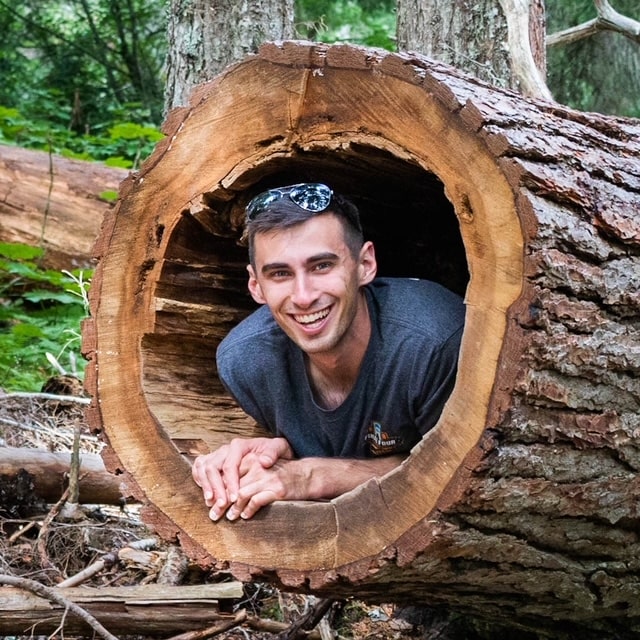 A photo of Dom, one of the Forever and Evergreens Photographers, in a log in Glacier National Park.