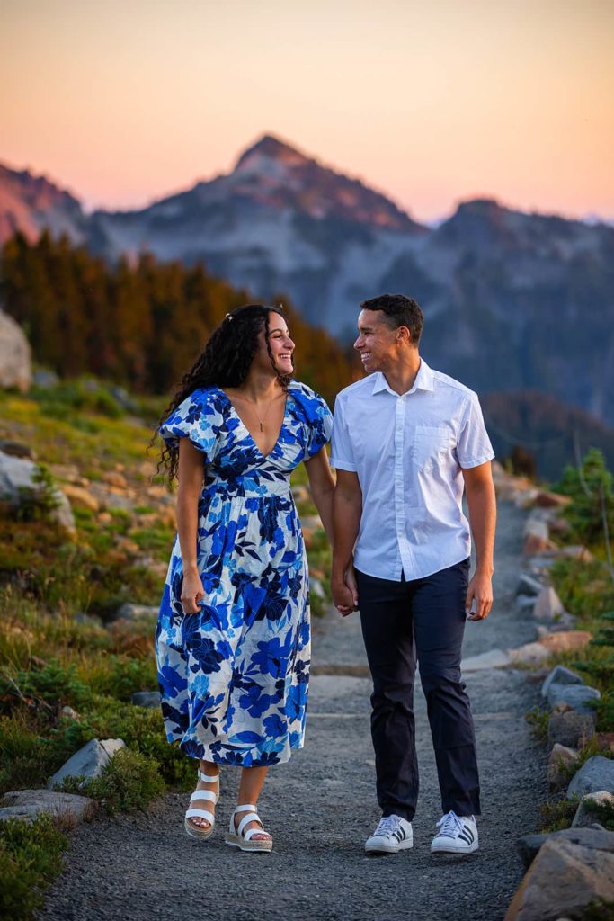 A couple smiles at one another as they walk down a gravel path at Mount Rainier National Park during their September engagement photos.