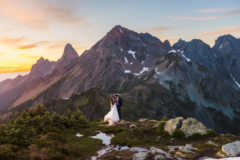 A bride and groom stand in front of a stunning mountain during sunset. The incredible scenery for their wedding makes it clear that they picked an epic place to elope.