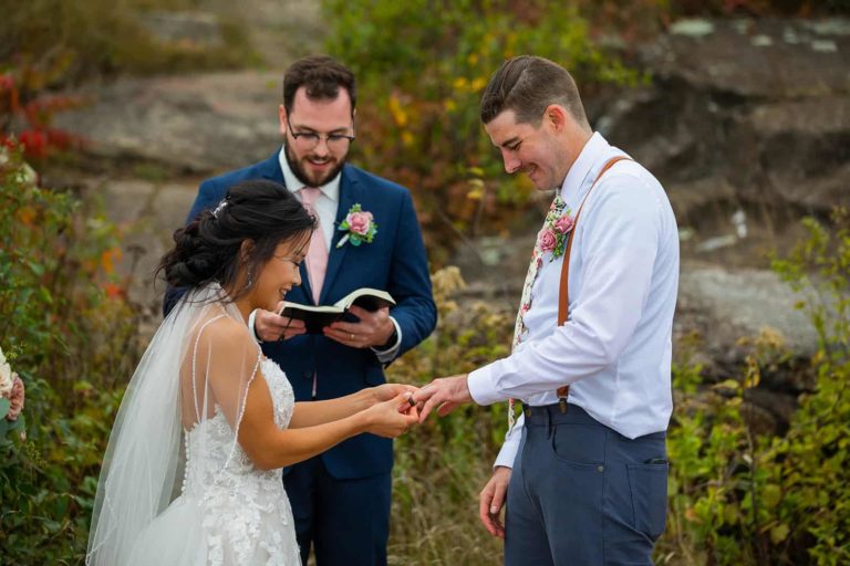 A bride and groom exchange rings during their wedding ceremony in front of a fall backdrop during their northern Minnesota elopement in Duluth.