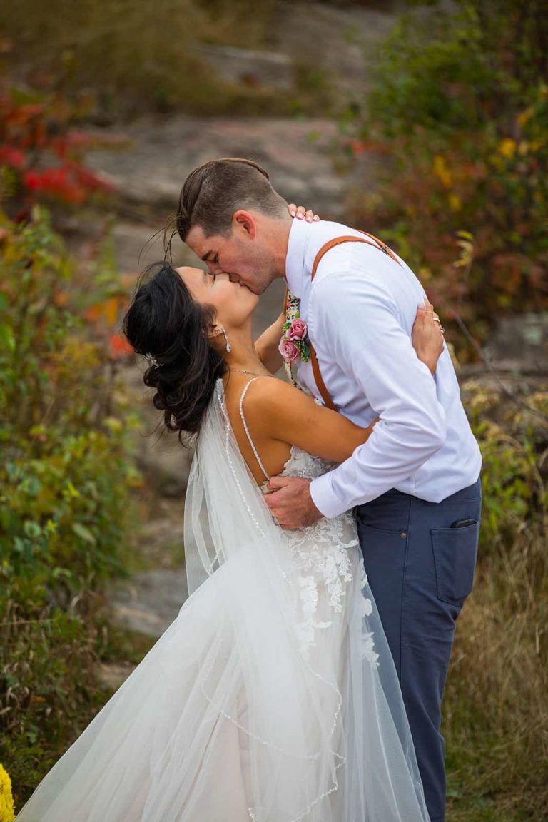 A bride and groom share their first kiss in front of a fall backdrop during their northern Minnesota elopement in Duluth.