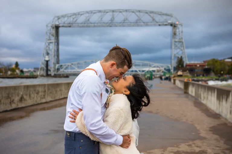 A bride and groom embrace in front of the Duluth Lift Bridge during their Midwest elopement in northern Minnesota.