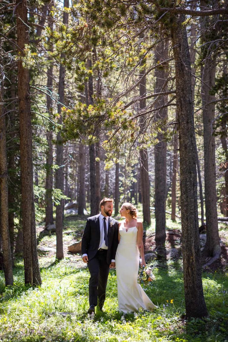 A bride and groom walk through a pine forest on their elopement day with Forever and Evergreens Adventure Elopement Photography.