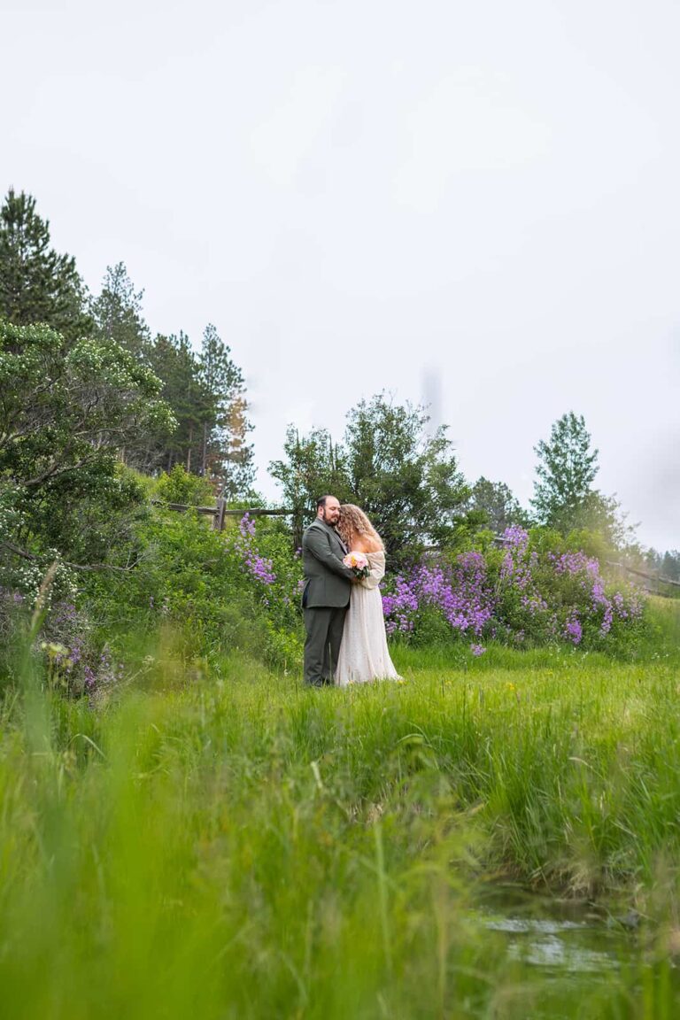 A bride and groom embrace in a grassy field near a little creek during their Black Hills elopement.