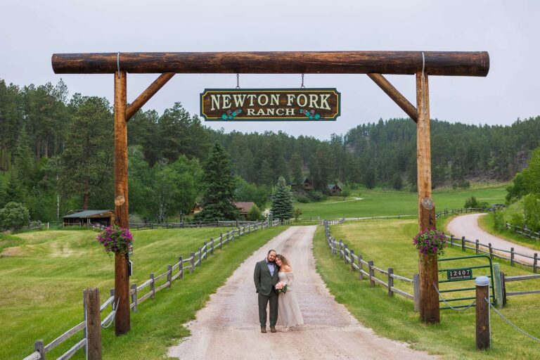 A couple stand under the Newton Fork Ranch sign during their Black Hills elopement.