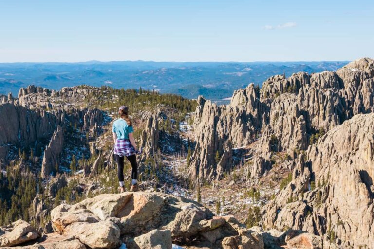 A woman stands on a rocky outcropping overlooking the dramatic rock formations of the Black Hills in South Dakota.