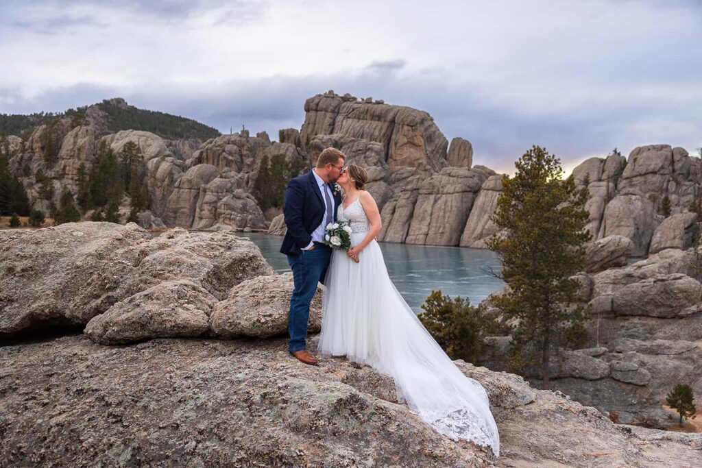 During their Hill City, South Dakota elopement, a couple shares a kiss on the rocky shore of Sylvan Lake in Custer State Park.