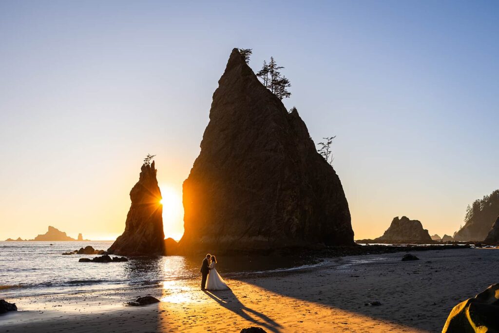 A couple embrace in a beam of sunlight streaming between two large rocks on the beach during their Washington adventure elopement in Olympic National Park.