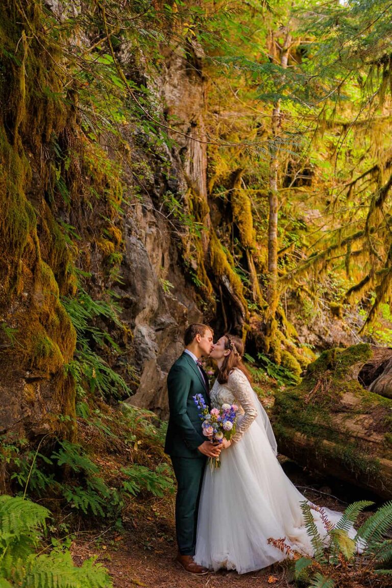 A bride and groom kiss during their elopement in a mossy Washington forest.