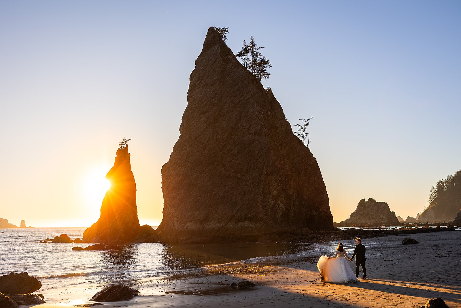 A bride and groom walk along the Washington Coast in Olympic National Park glowing golden with the setting sun during their elopement with Forever and Evergreens.