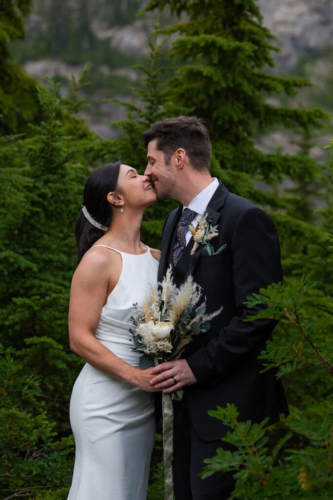 A bride and groom share a kiss among a grove of pine trees during their elopement in Washington state.