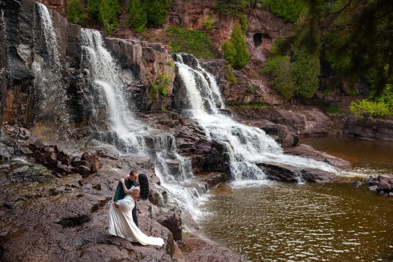 A bride and groom pose for a photo in front of a waterfall during their Minnesota elopement.