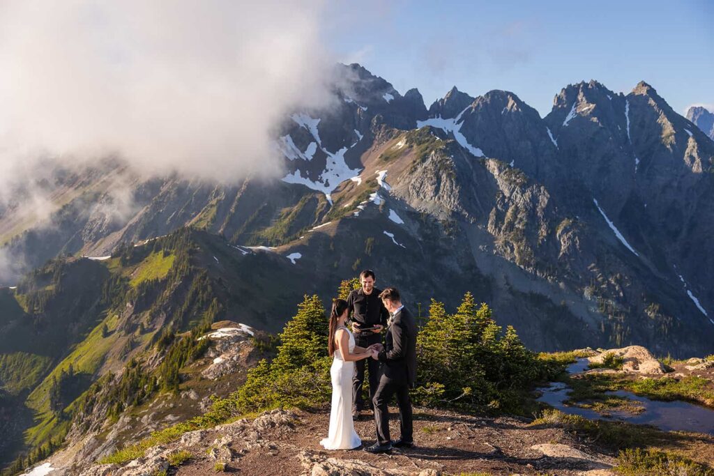 A couple stand in front of an epic mountain during the adventure elopement while Dom from Forever and Evergreens performs their wedding ceremony as their officiant.