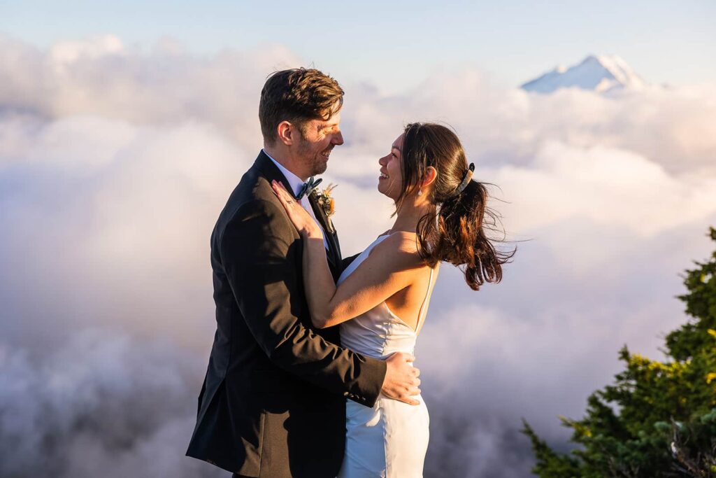A couple stand in front of a cloud inversion with the peak of Mount Baker peaking out of the clouds behind them during their mountain elopement.