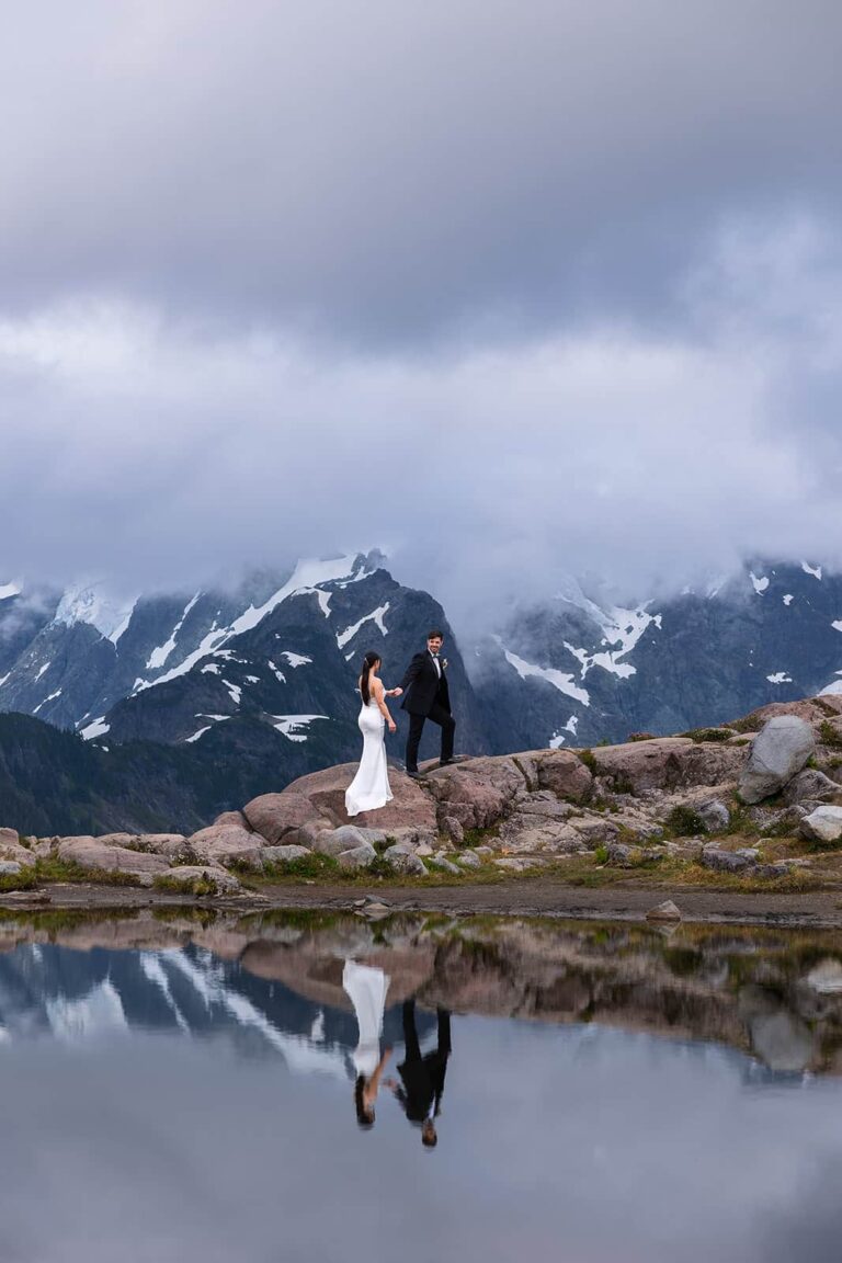 A couple stand in front of a mountain with the reflection in a little pool of water during their mountain elopement.