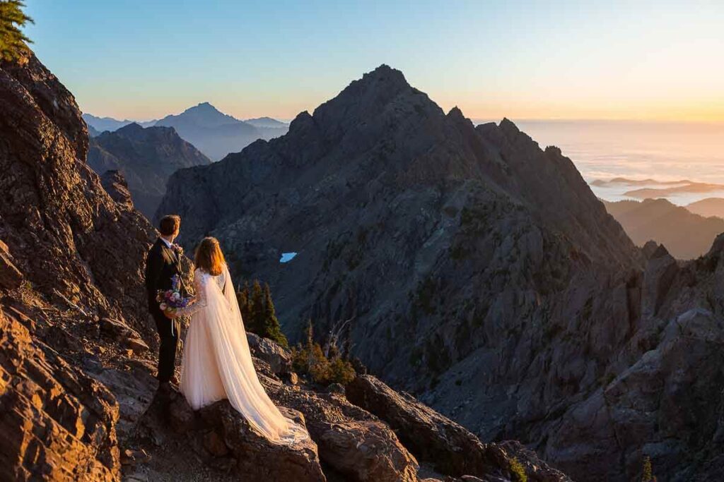 A bride and groom looking out at the sunrise from the top of Mount Ellinor during their hiking elopement.