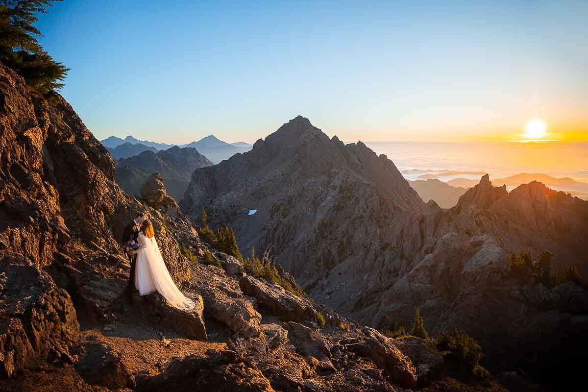 An epic sunrise from the top of Mount Ellinor with a couple in their wedding clothes posing on the side of the mountain.