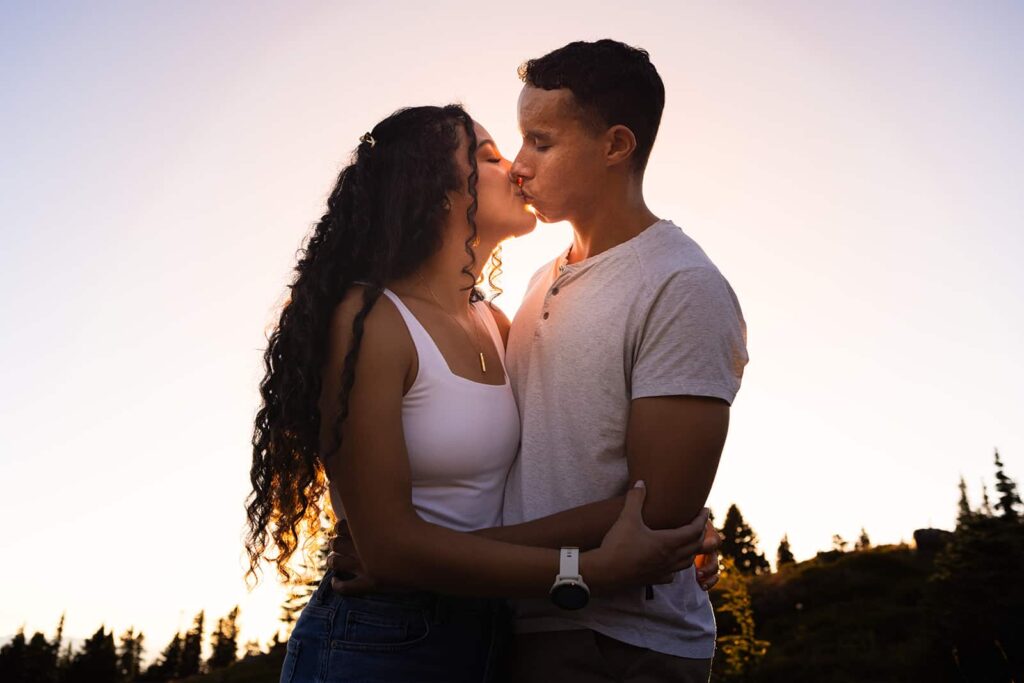 A young couple kiss in front of the setting sun during their engagement photo session.