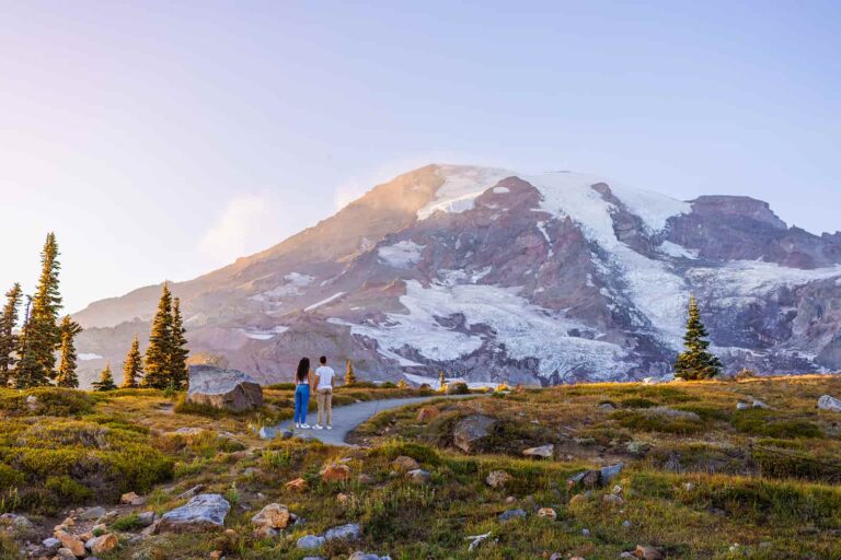 A couple stand on a trail and stare at Mount Rainier with awe and wonder.
