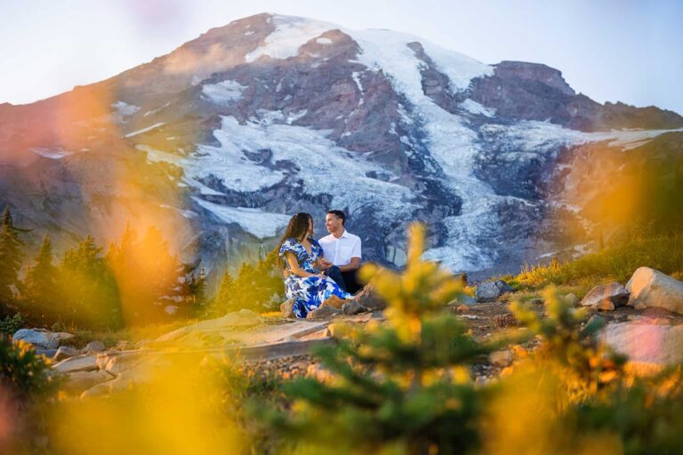 An engaged couple cuddles up in front of Mount Rainier on a sunny September evening for their engagement photo session in the park.