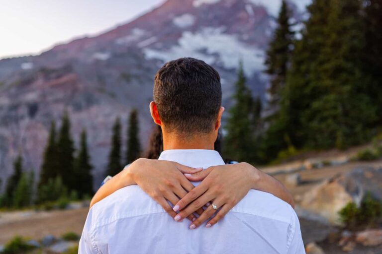 A close up of a woman's hands over the shoulders of her finance during their engagement shoot in the Paradise area of Mount Rainier NP.