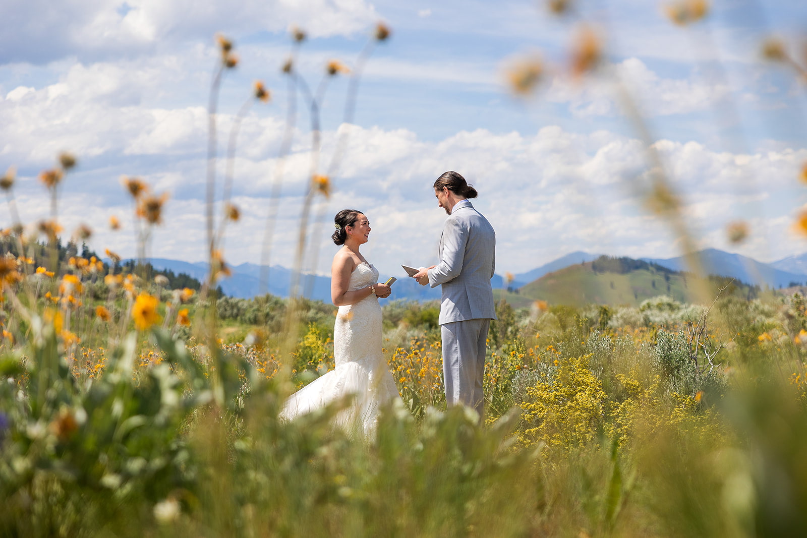 A bride and groom stand in a field of balsamroot flowers while exchanging vows during their elopement in Twisp, WA.