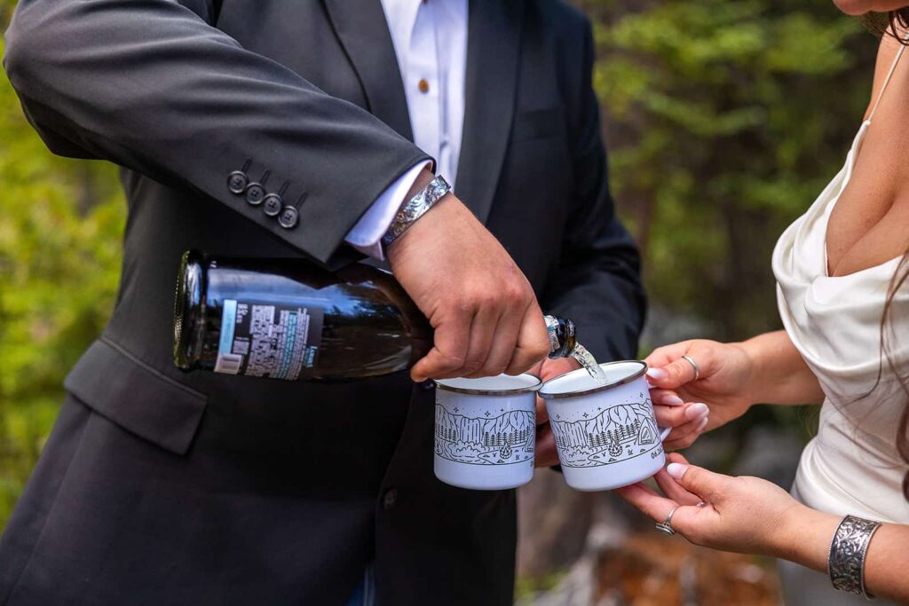 A groom pours champagne into a custom wedding mug during an adventure elopement.