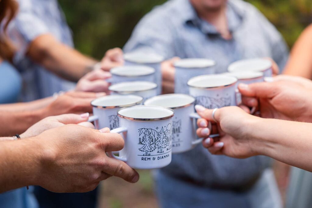 A group of people do a cheers with their custom adventure wedding mugs.